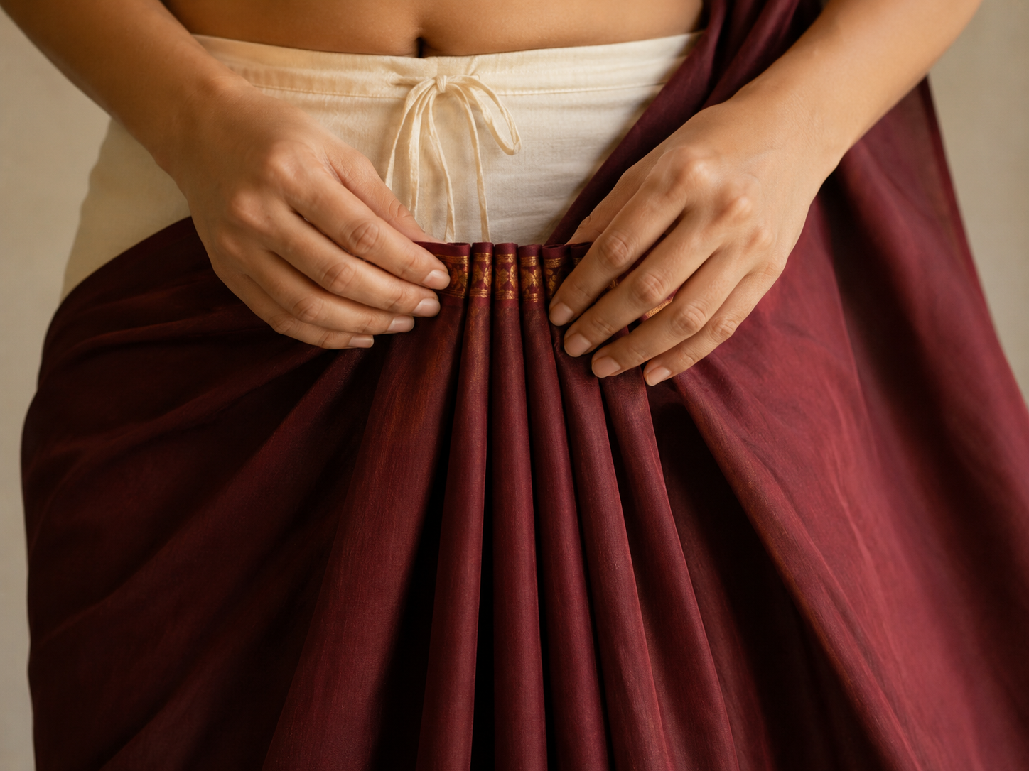 Hands gathering even fan-like pleats in a saree at the front centre of the body before tucking