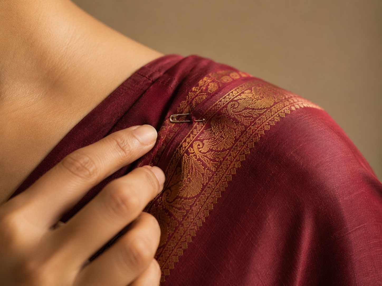 A small safety pin securing a saree pallu at the shoulder seam with the final draped saree in view