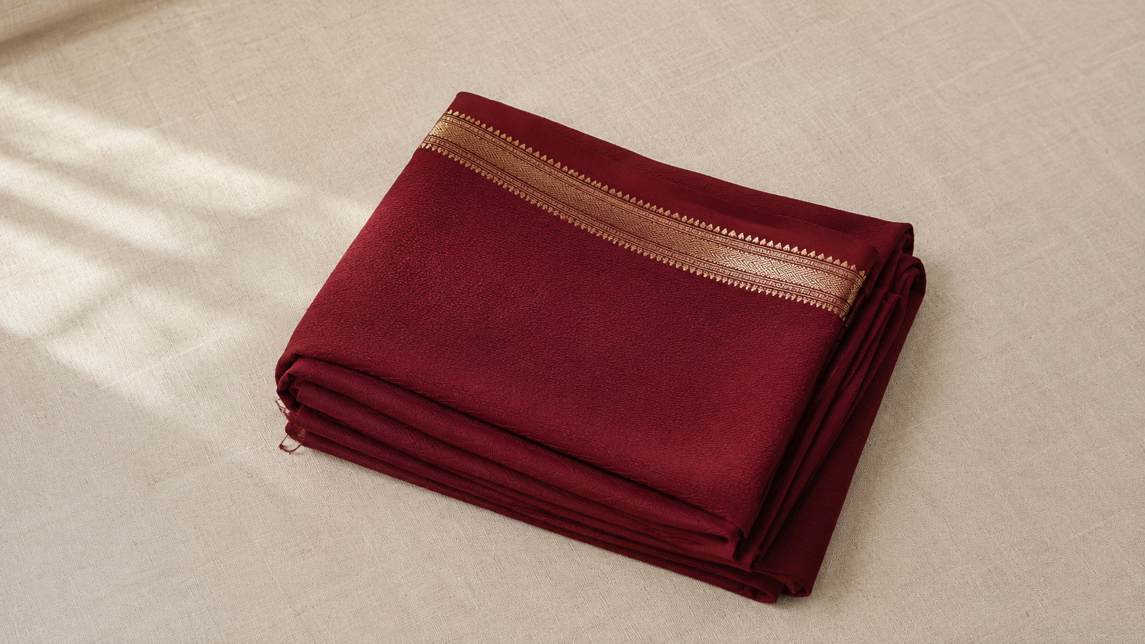 A folded georgette saree in deep wine red showing the fabric's characteristic fluid texture