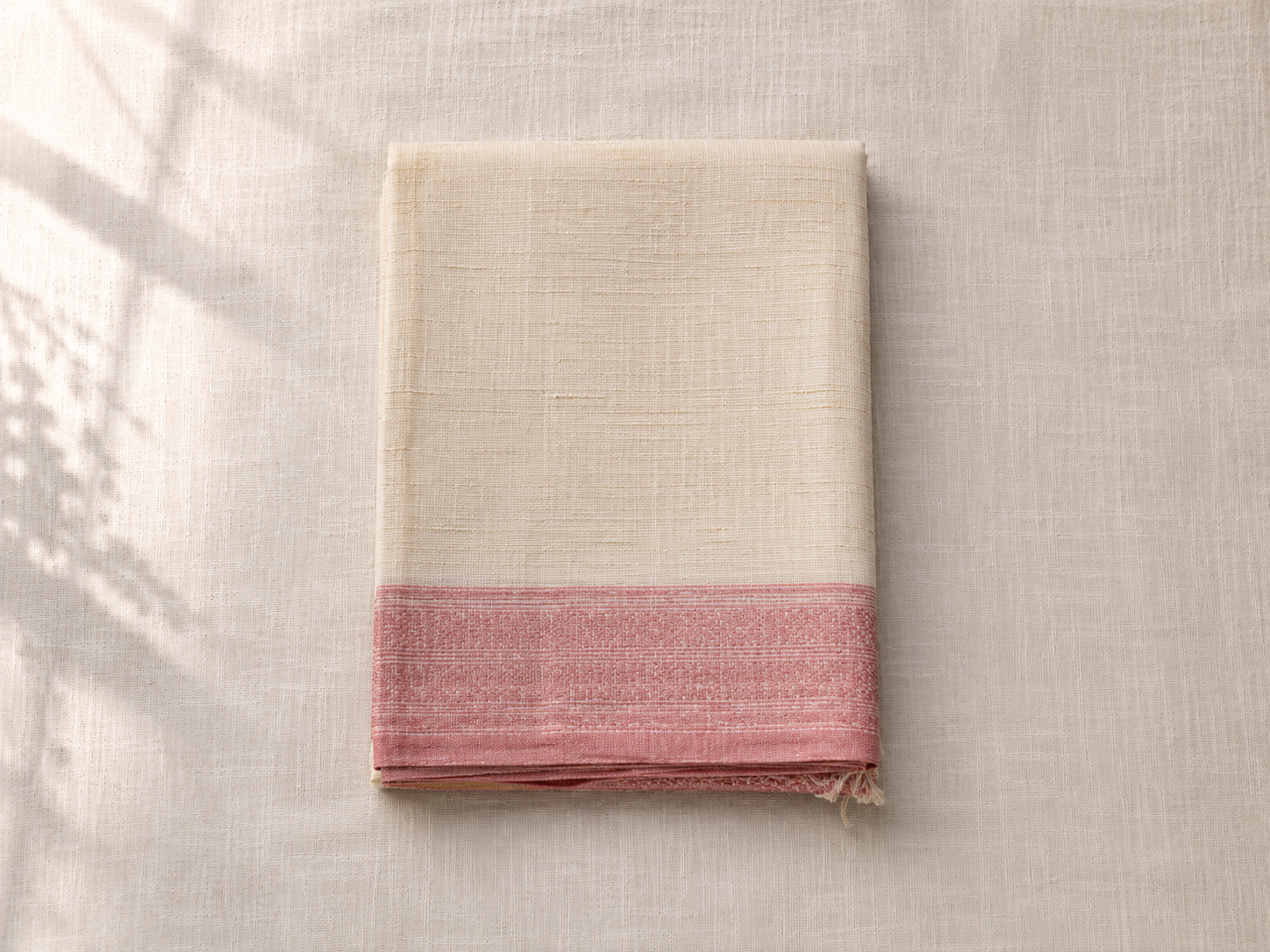 A folded handloom cotton saree in cream and dusty pink with a simple woven border