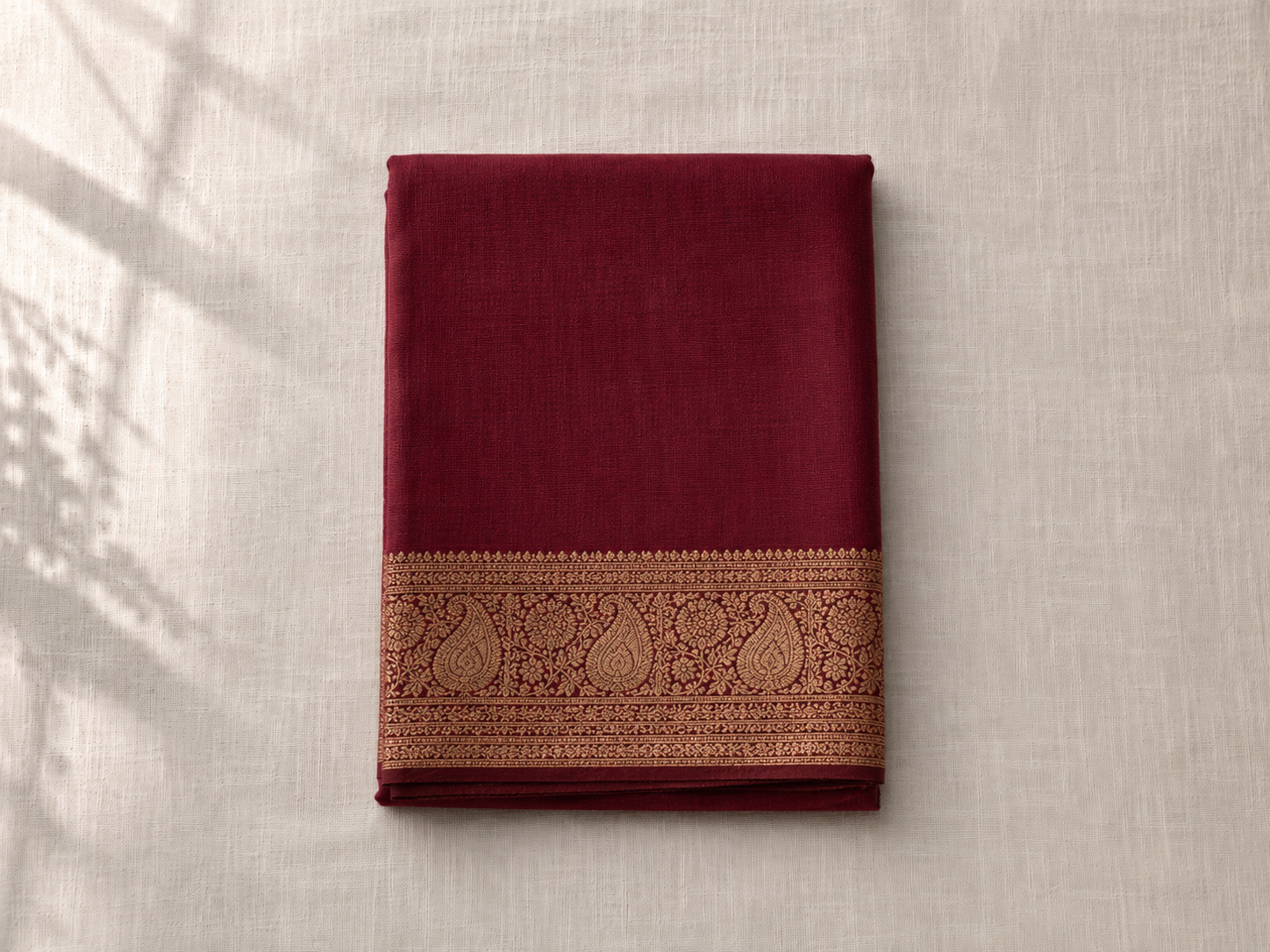 A folded deep maroon Banarasi silk saree with intricate gold zari brocade visible at the border