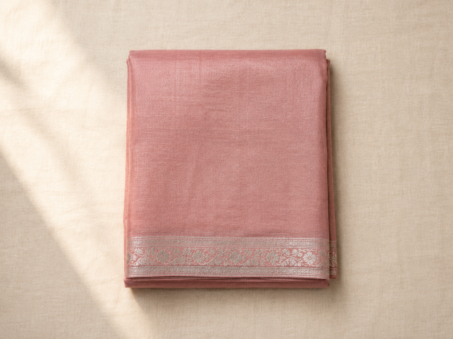 A folded soft dusty rose Chanderi saree with a delicate silver border in winter light