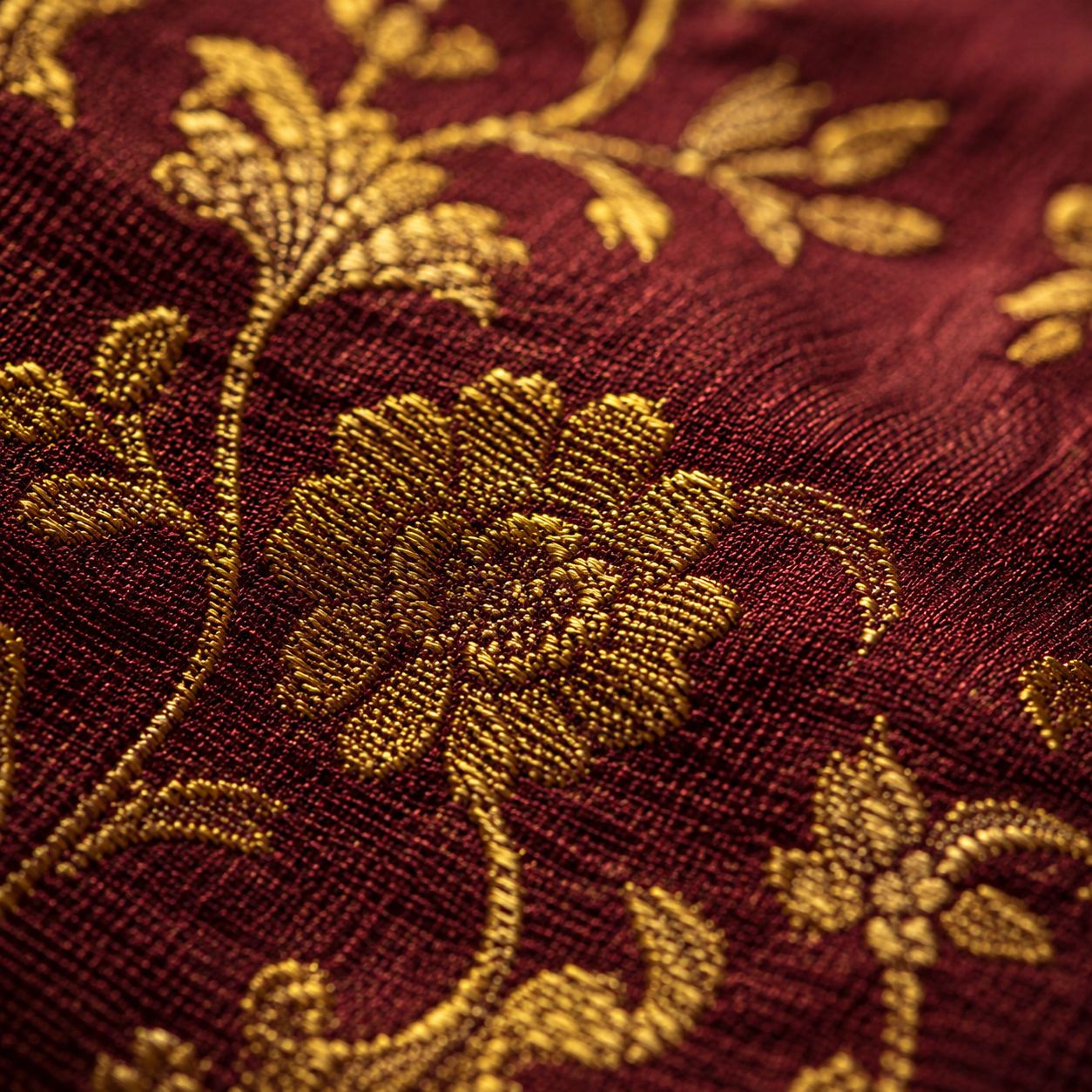 Extreme close-up of gold zari thread woven into deep maroon Banarasi silk fabric
