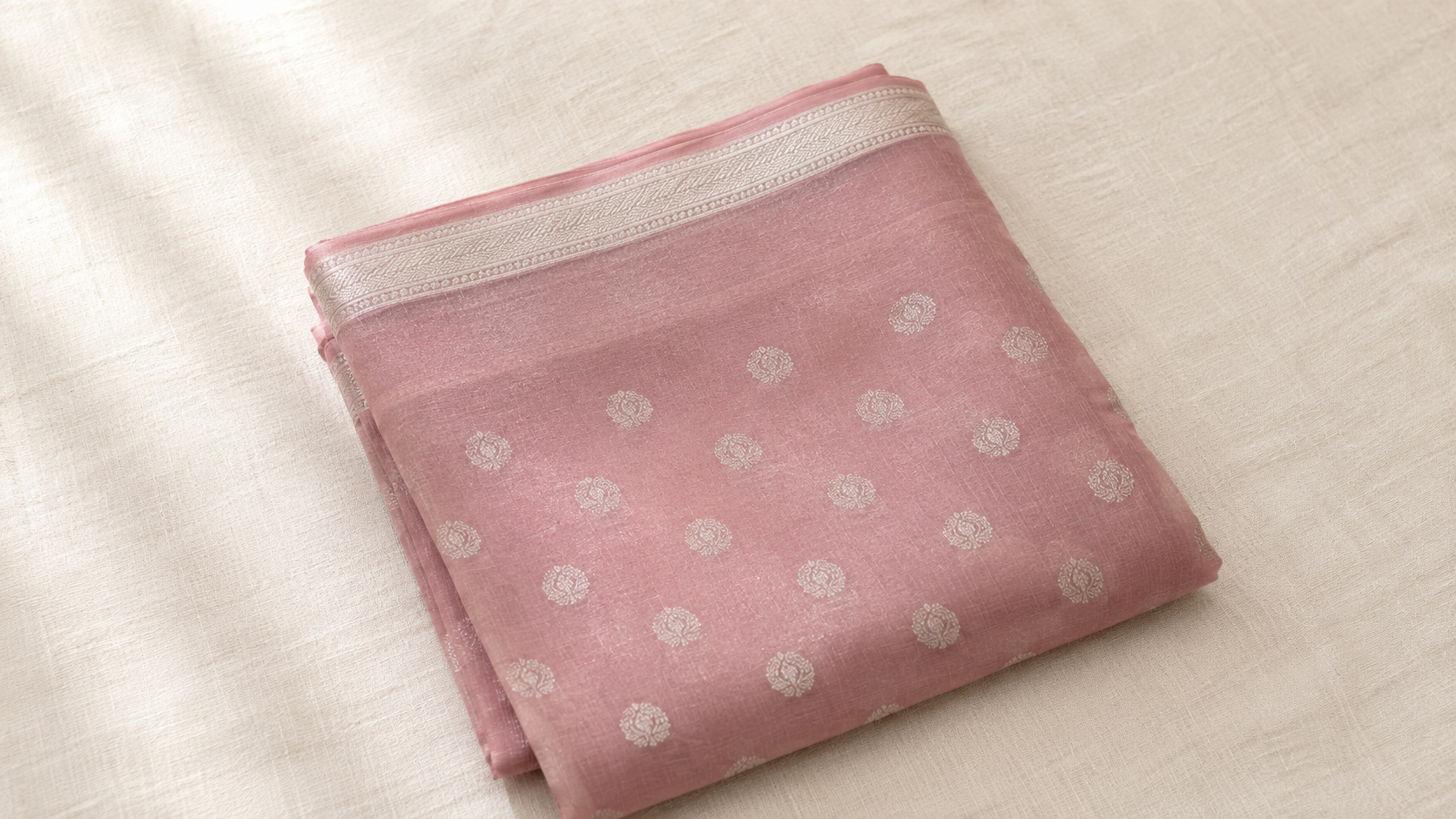 A folded Chanderi saree in soft dusty rose with delicate silver zari motifs along the border