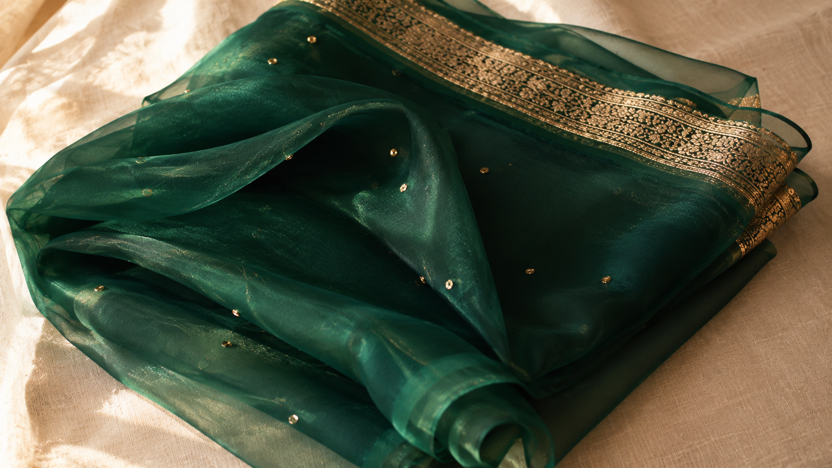 A folded chiffon saree in deep emerald green showing the fluid sheer drape character